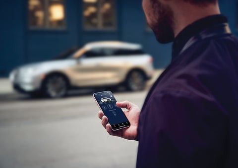 A person is shown interacting with a smartphone to connect to a Lincoln vehicle across the street. | Jenkins & Wynne Lincoln in Clarksville TN