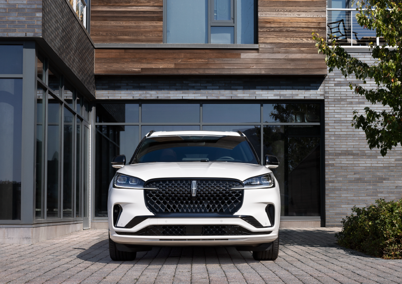 A white 2025 Lincoln Aviator® SUV is shown parked outside a modern building with gray brick and wood accents. | Jenkins & Wynne Lincoln in Clarksville TN