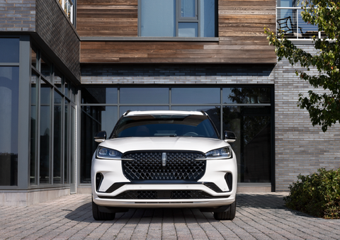 A white 2025 Lincoln Aviator® SUV is shown parked outside a modern building with gray brick and wood accents. | Jenkins & Wynne Lincoln in Clarksville TN