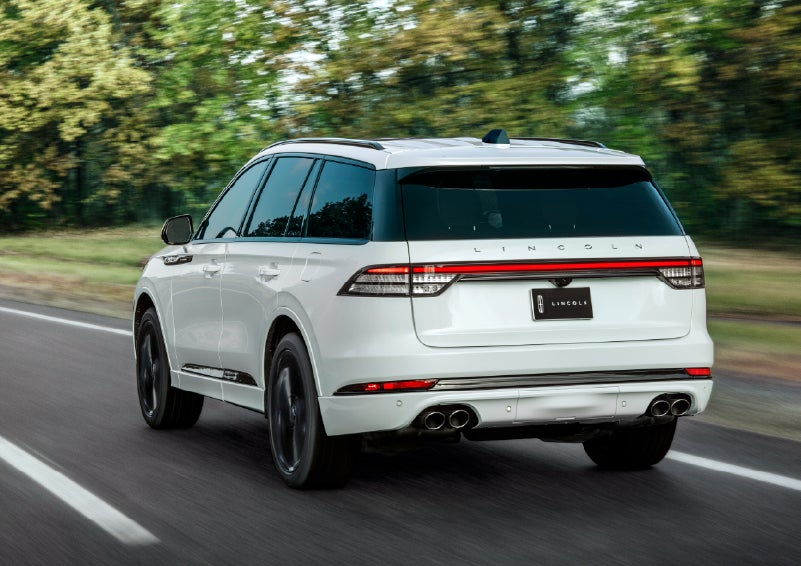 A white 2026 Lincoln Aviator® SUV is being driven away down a road lined with colorful trees. | Jenkins & Wynne Lincoln in Clarksville TN