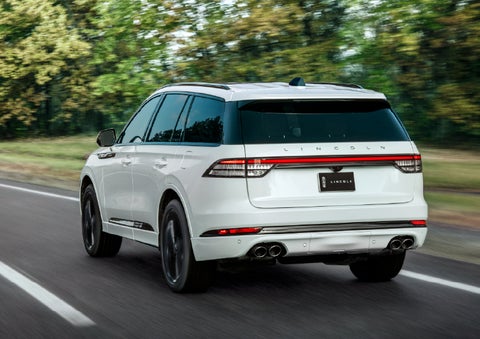 A white 2026 Lincoln Aviator® SUV is being driven away down a road lined with colorful trees. | Jenkins & Wynne Lincoln in Clarksville TN